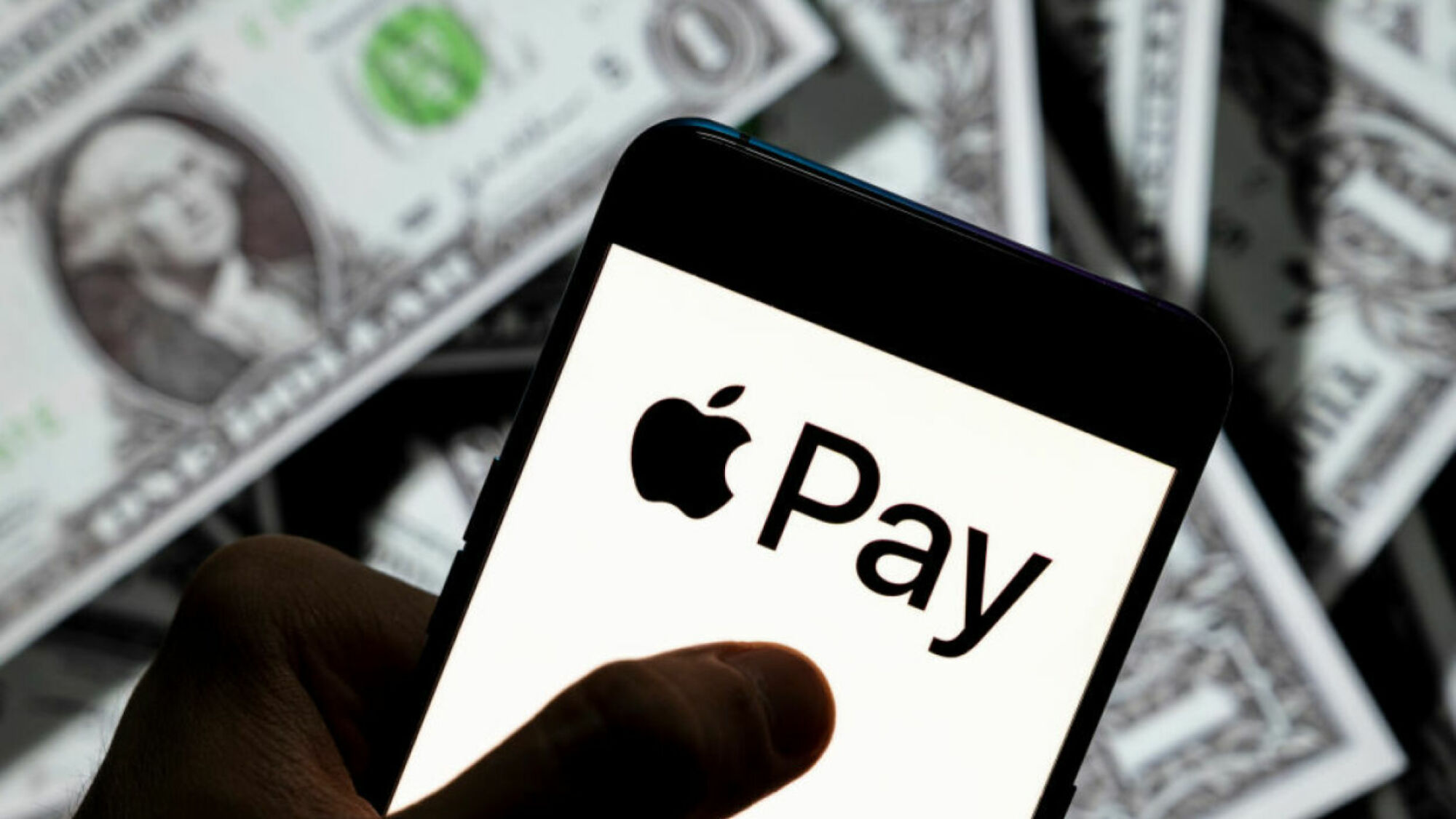 Teléfono inteligente negro con el logotipo de Apple Pay en la pantalla.  El fondo está lleno de billetes de $1. 