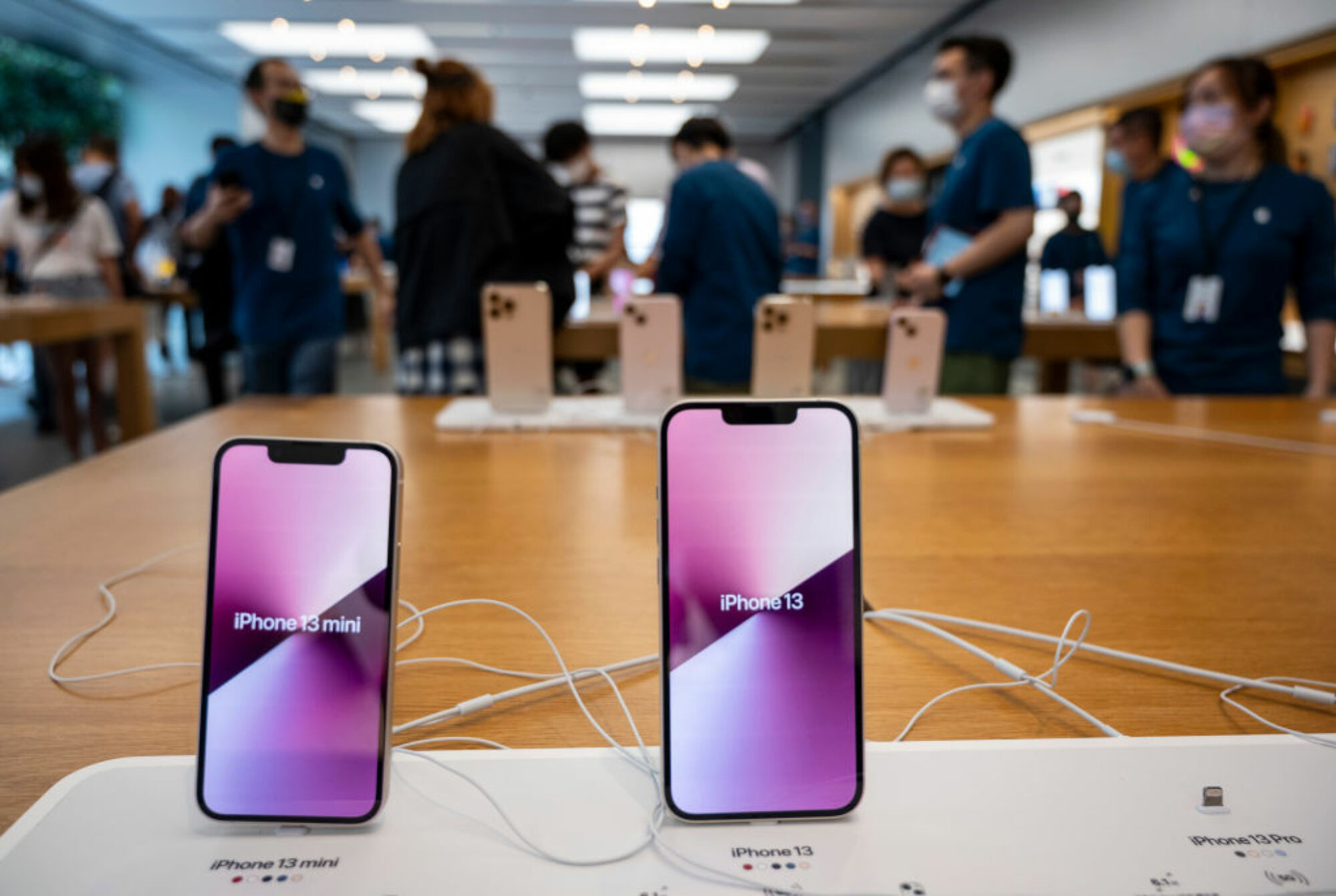 Dos iPhones en la tienda de Apple con sus nombres en la pantalla.  iPhone 13 mini a la izquierda, iPhone 13 a la derecha.
