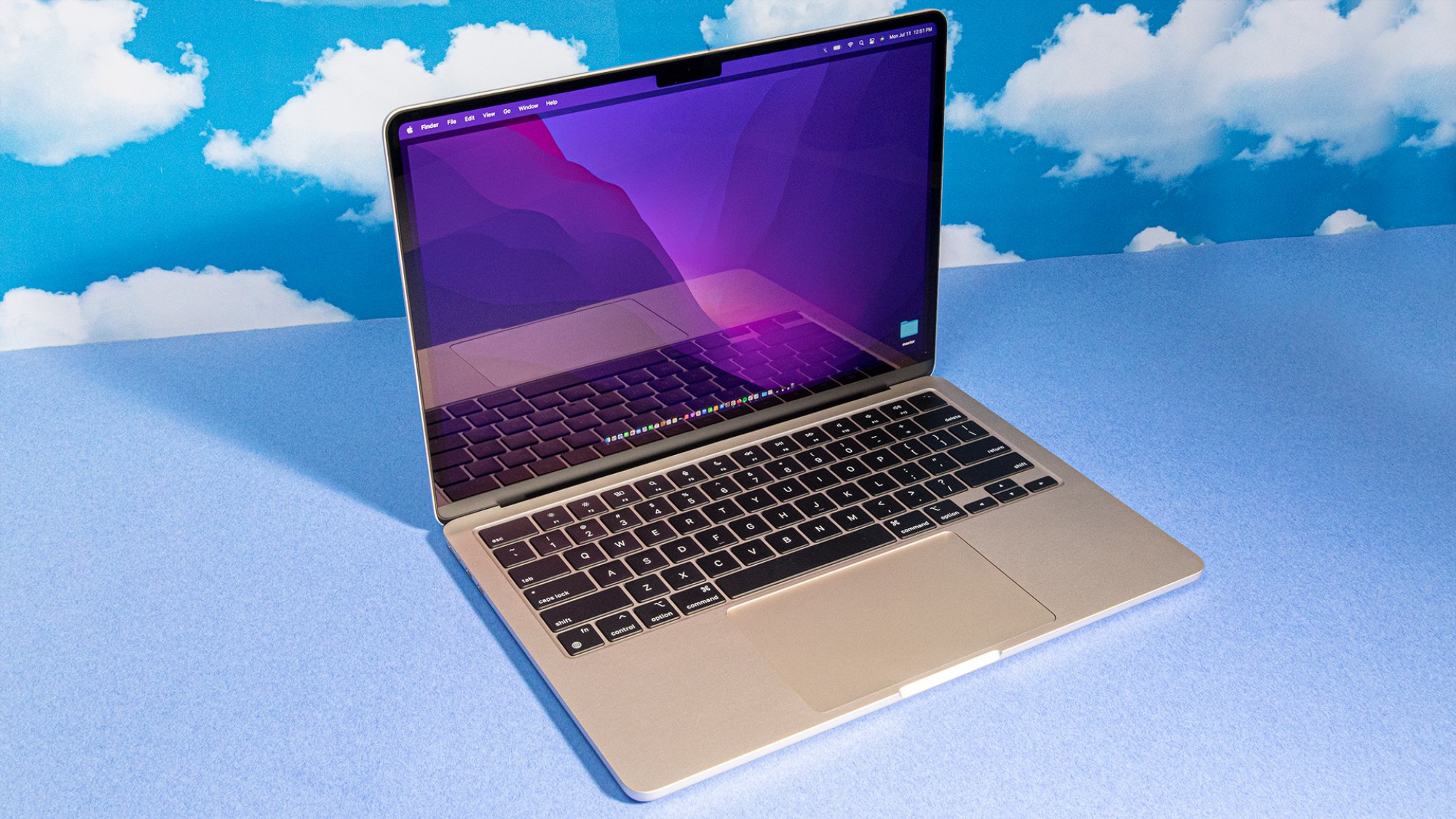 MacBook Air 2022 M2 en vista de perfil contra un fondo azul con patrones de nubes repetitivos